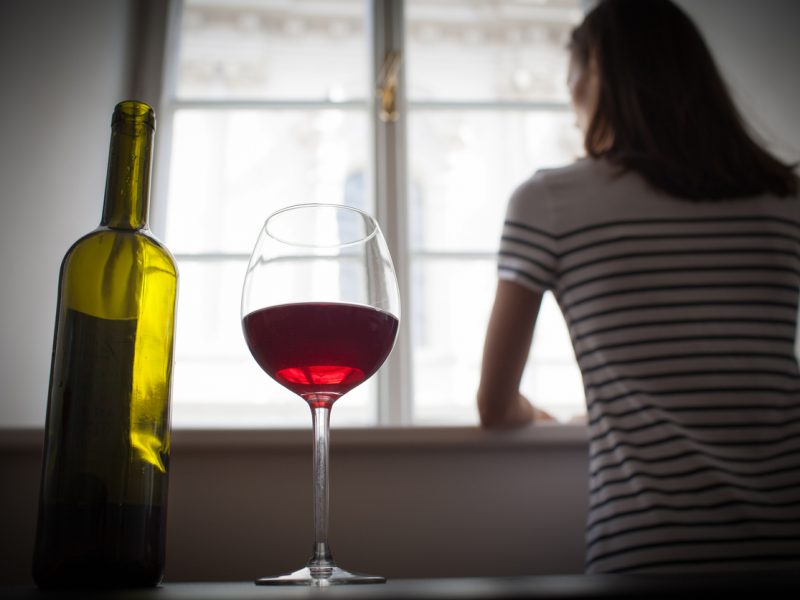 Imatge d'arxiu d'una dona mirant per la finestra i una botella de vi.