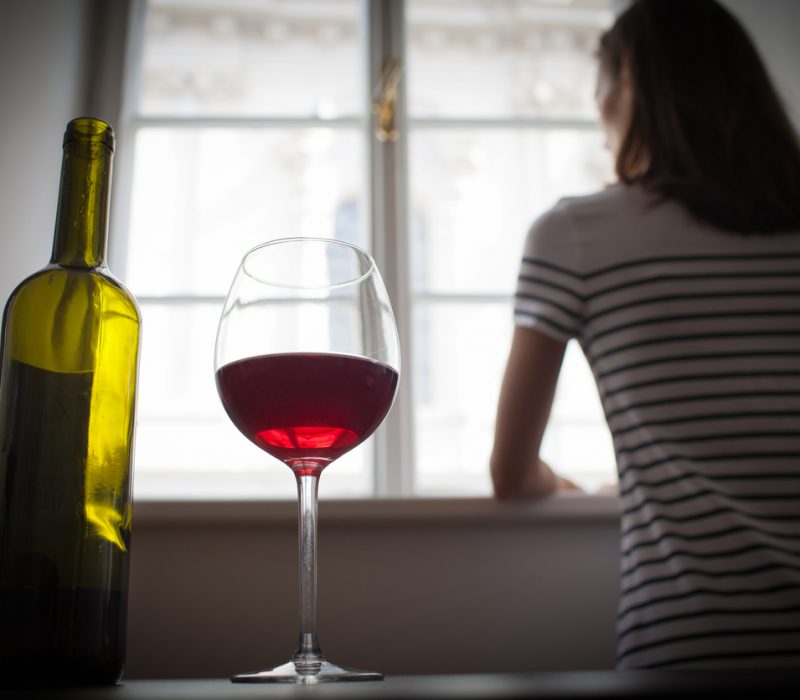 Imatge d'arxiu d'una dona mirant per la finestra i una botella de vi.